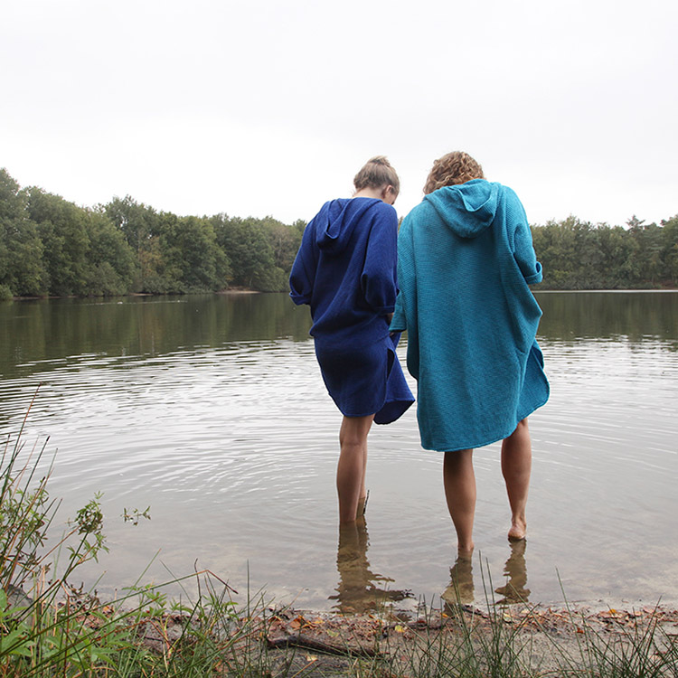 Twee dames in een omkleed poncho van zeemeermantel® staan met hun voeten in het water van een bosmeer